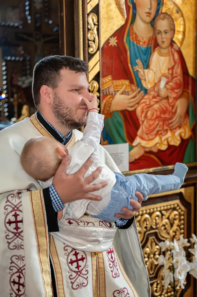 Preotul ține pruncul în brațe, în fața icoanei Maicii Domnului
