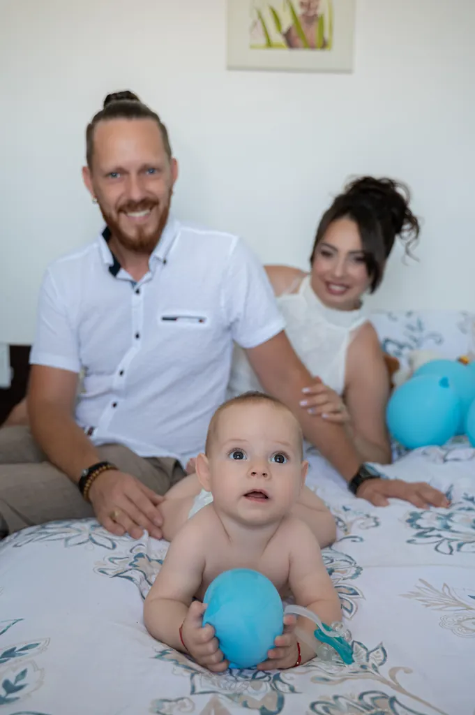 Părinții zâmbesc lângă bebelușul care se joacă cu un balon albastru