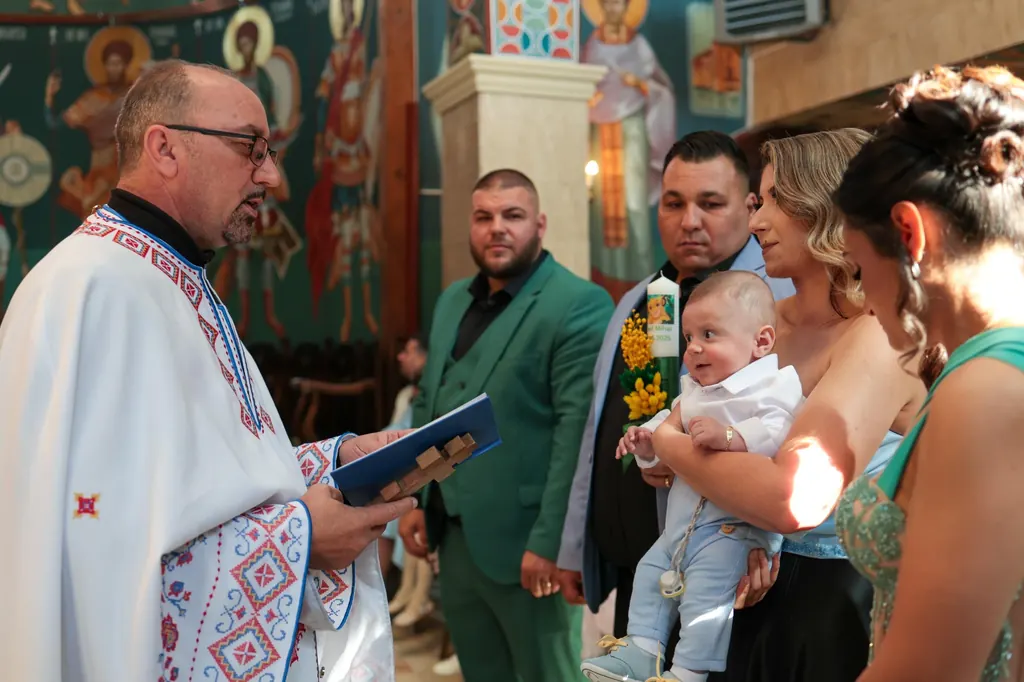 Preotul citește rugăciunile, în timp ce copilul este ținut în brațe de familie