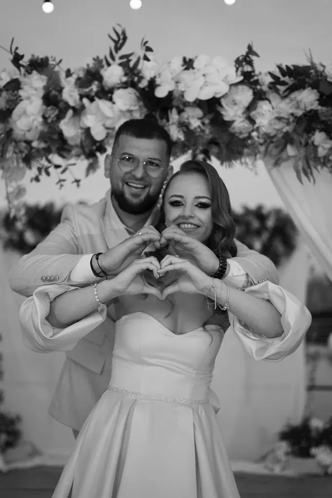 Mirii fac o inimă din mâini sub arcada florală