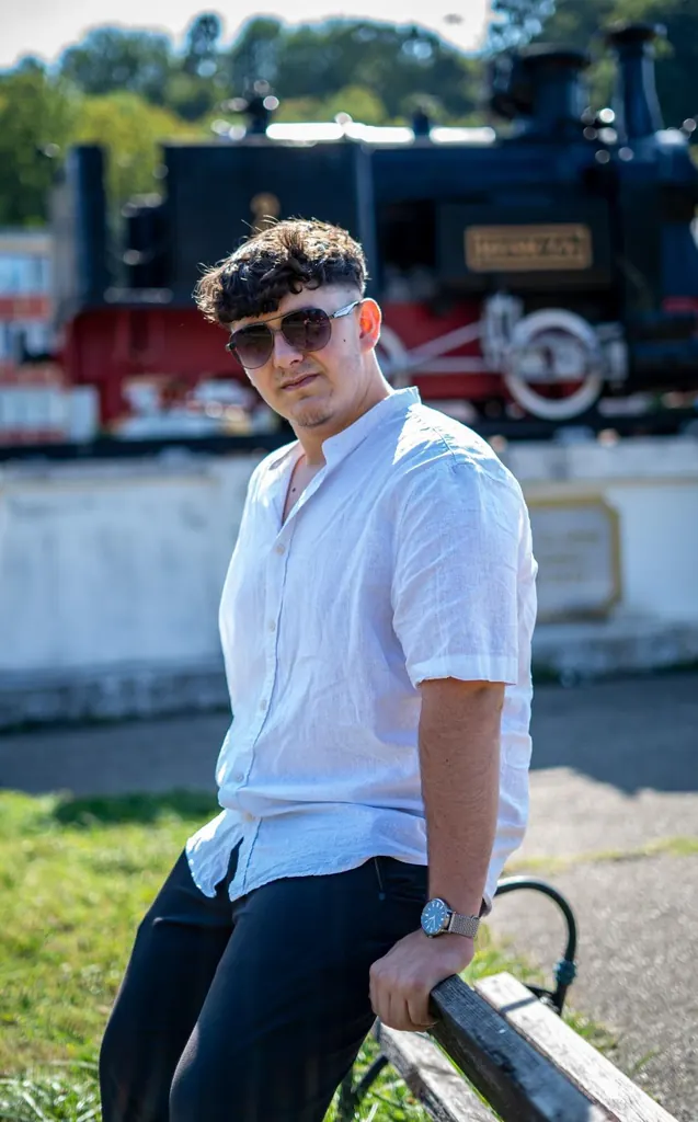 Tânăr așezat pe o bancă în fața unei locomotive cu abur